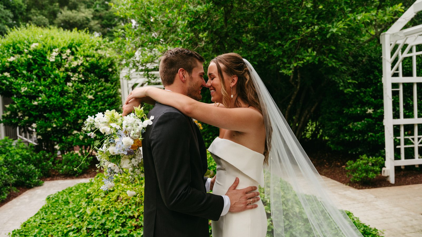 Hannah and Wesley embracing beside a white garden pergola at Covington Gardens