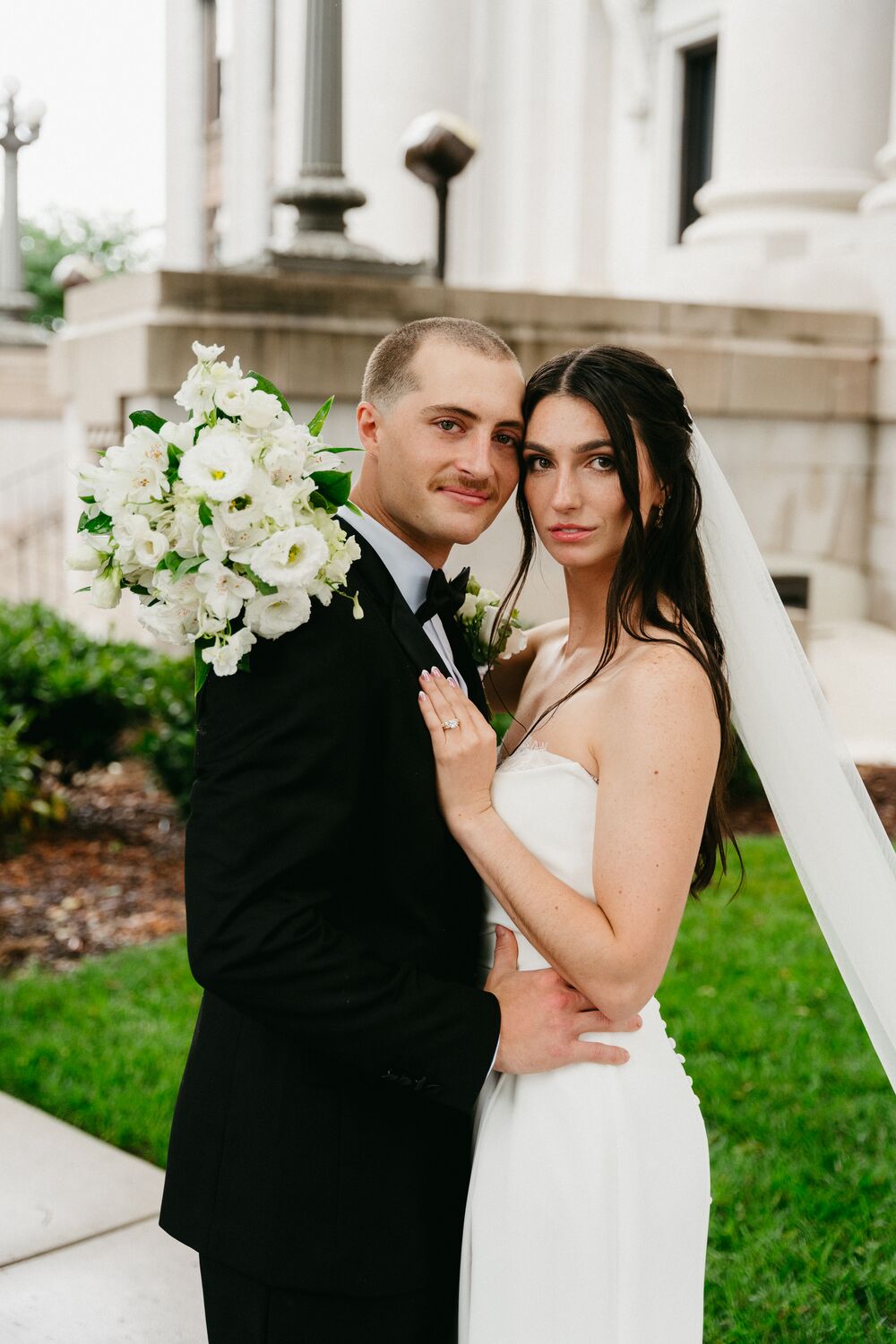 A bride and groom with a white bouquet outside the courthouse