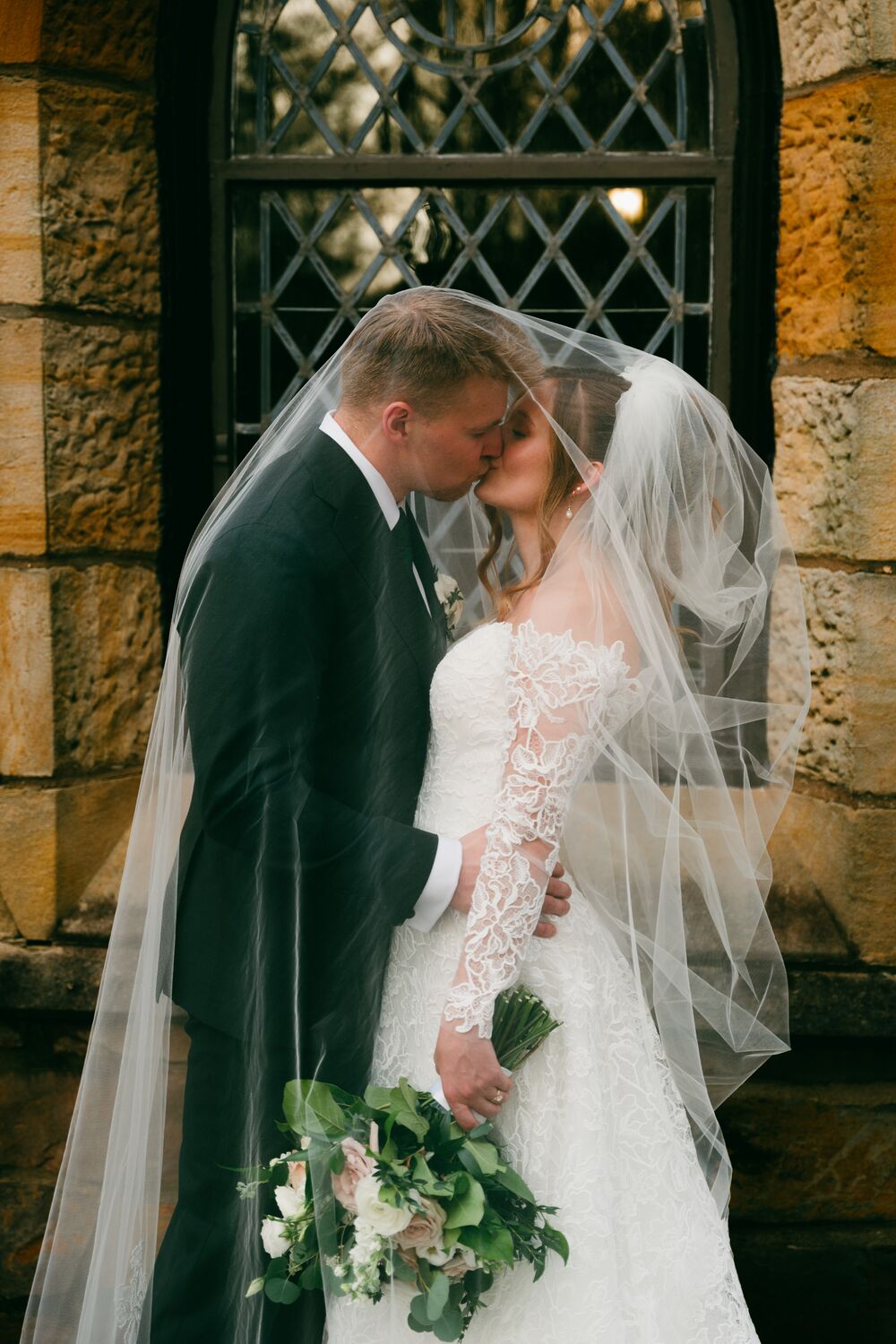 A kiss beneath the veil at a stone chapel
