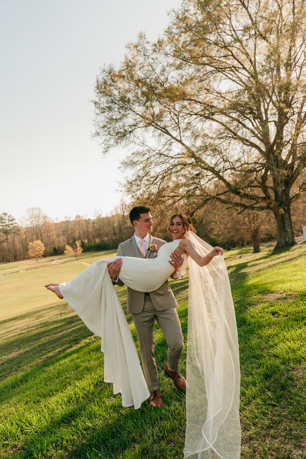 A groom joyfully carrying his bride across the lawn