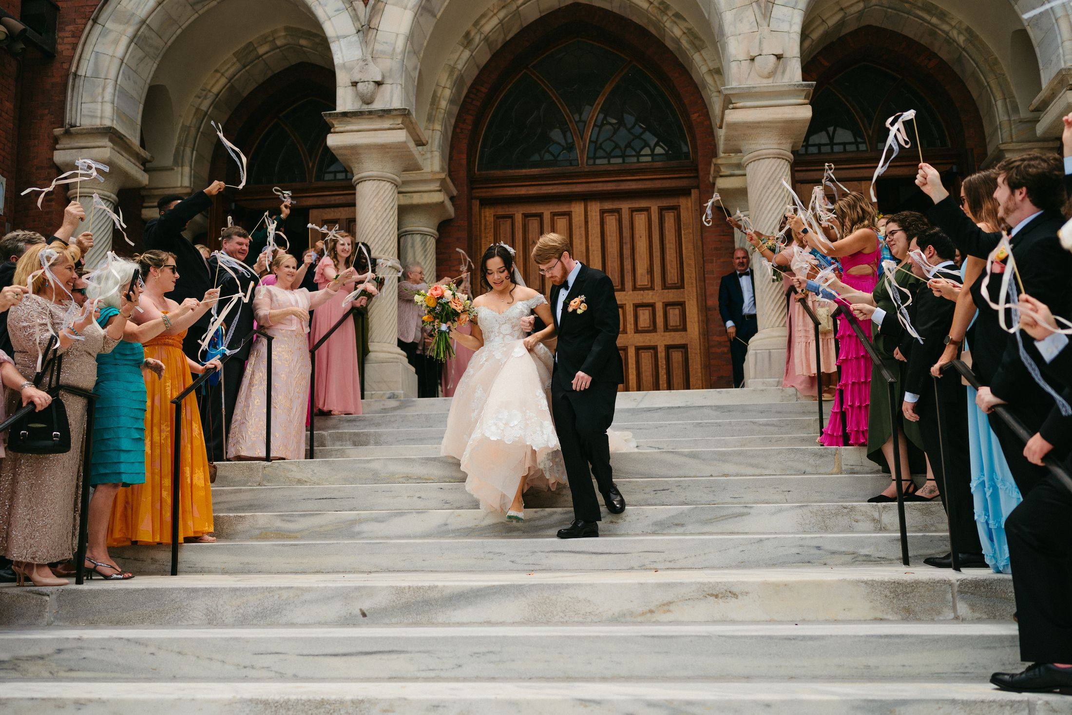 Brianna and Wesley exiting down the cathedral steps through ribbon wands