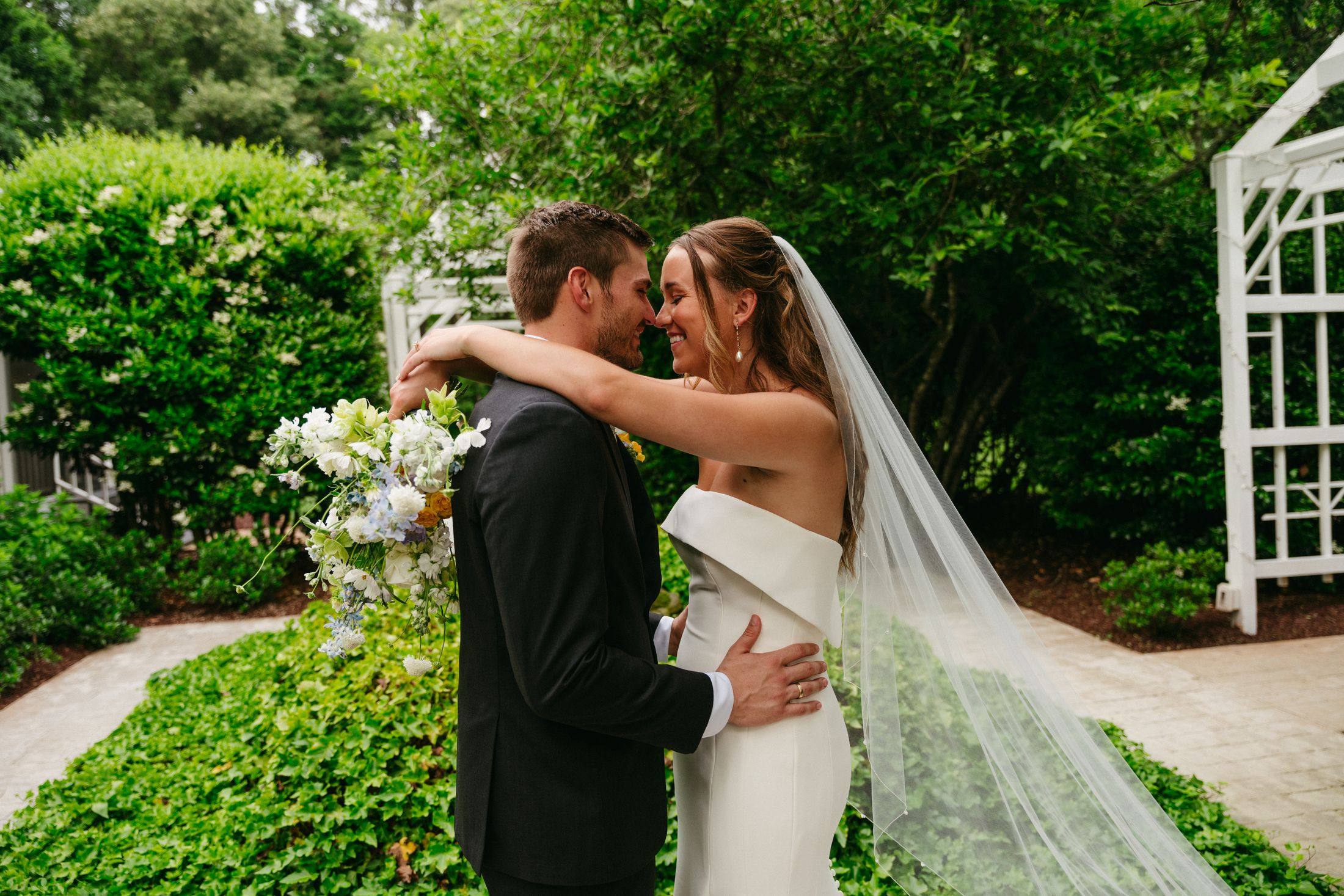 Hannah and Wesley embracing in the garden, her veil trailing behind