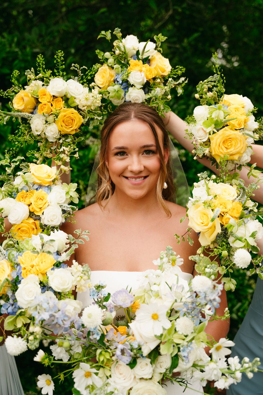 Hannah framed by yellow and white flowers held by her bridesmaids