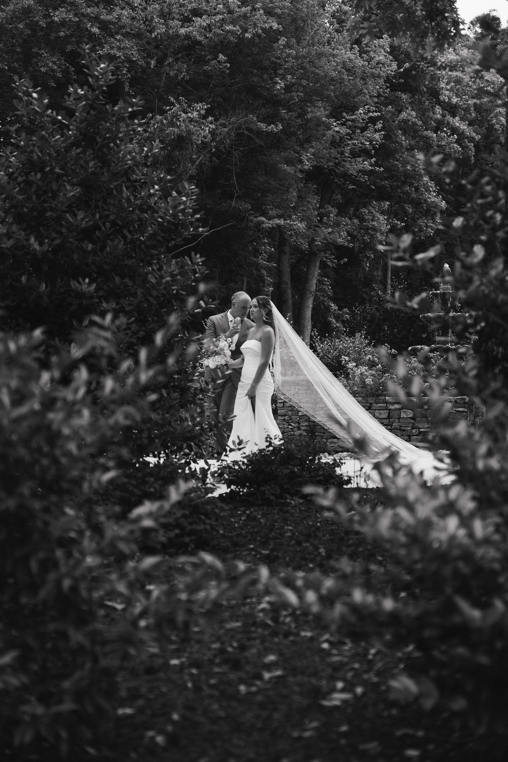 Hannah alone in the garden in black and white, veil spread behind her