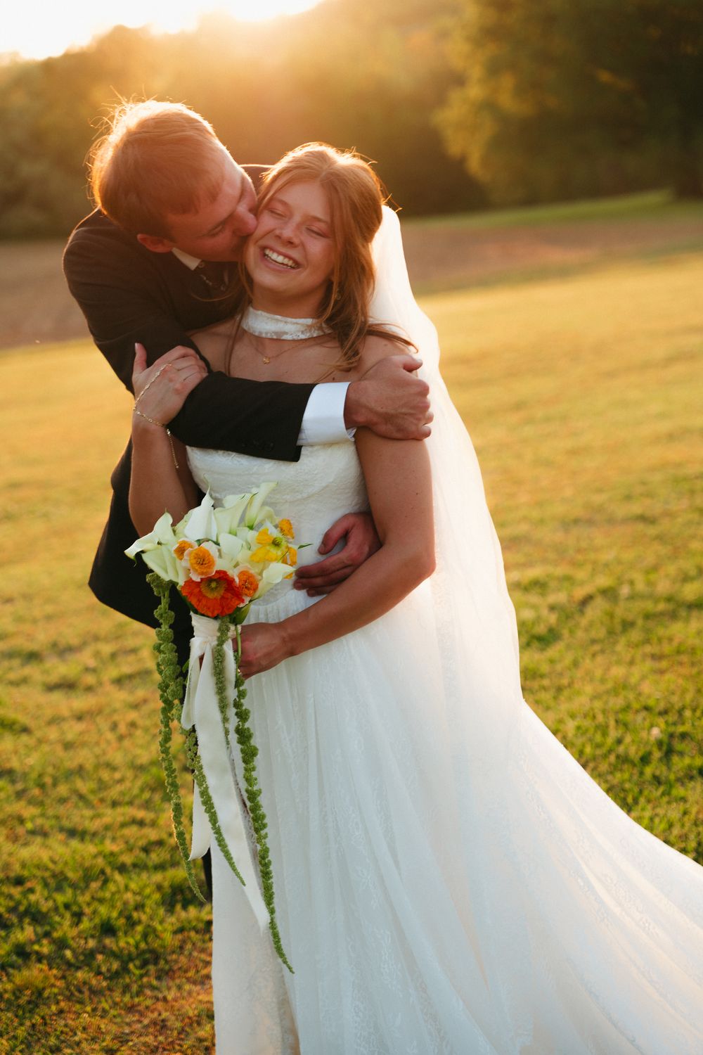 The groom embracing the bride in a golden-hour field