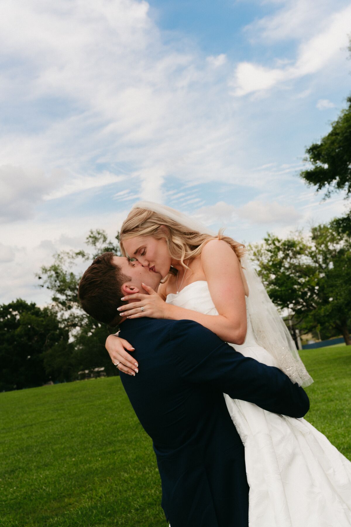 A groom dipping his bride for a kiss against an open sky